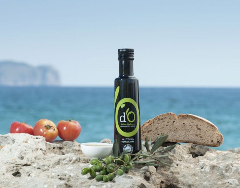 Botella de aceite de oliva de Mallorca junto a tomates y pan en la playa.