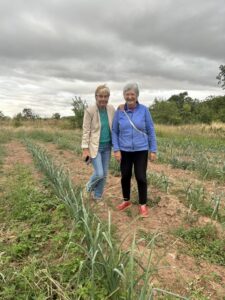 Dos mujeres posan entre hileras de plantas en un terreno cultivado.