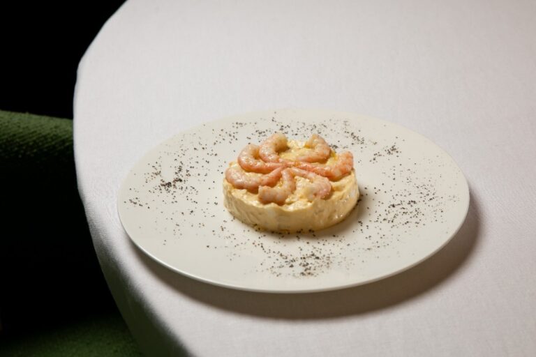 Ensaladilla rusa coronada con gambas sobre un plato blanco