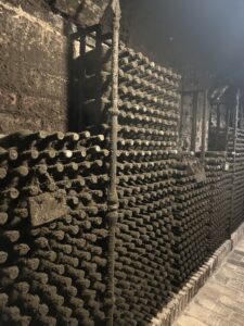 Filas de botellas colocadas en soportes dentro de una bodega oscura.