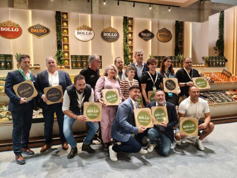 Grupo de personas posa con placas de Bollo frente a un expositor de frutas