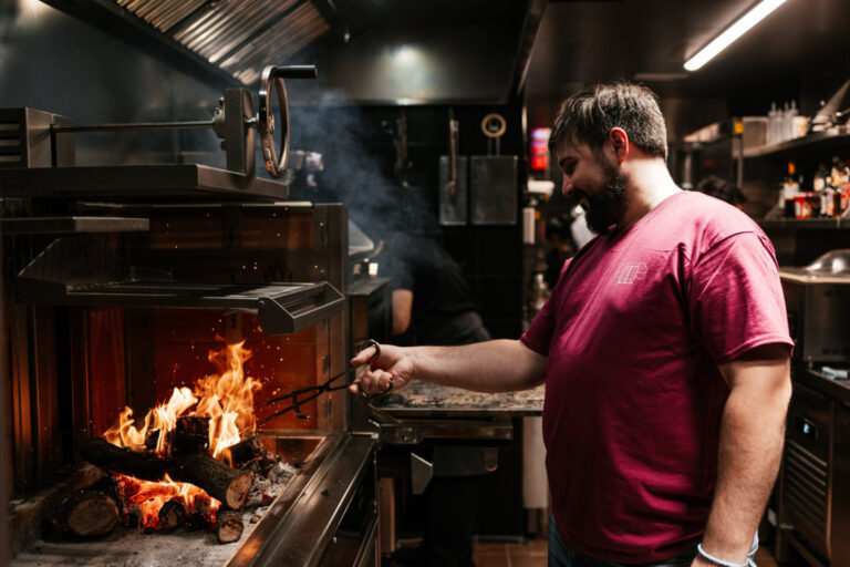 Hombre aviva el fuego de un horno de leña en una cocina.