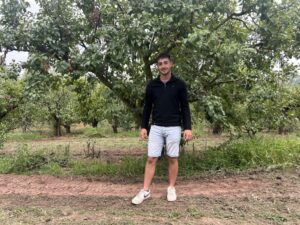 Un hombre está de pie entre árboles alineados en un terreno con vegetación.