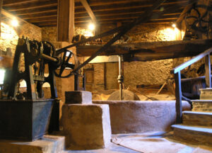 Interior de un molino antiguo con maquinaria, piedras de molienda y muros de piedra.