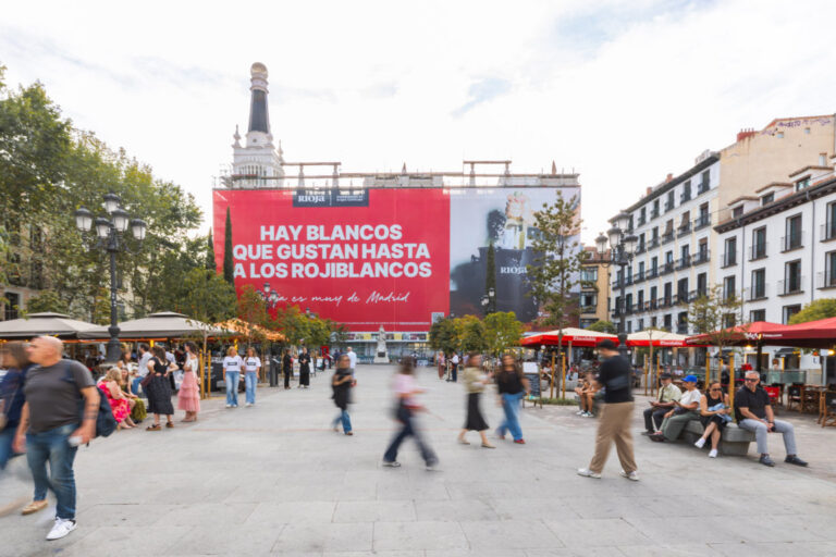 Gran lona publicitaria de Rioja en una plaza madrileña con peatones y terrazas