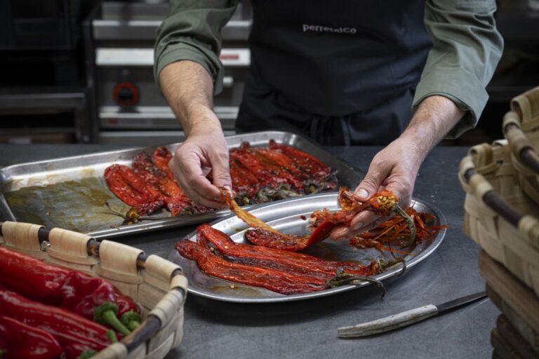 Manos pelan pimientos rojos asados sobre una bandeja en una cocina.