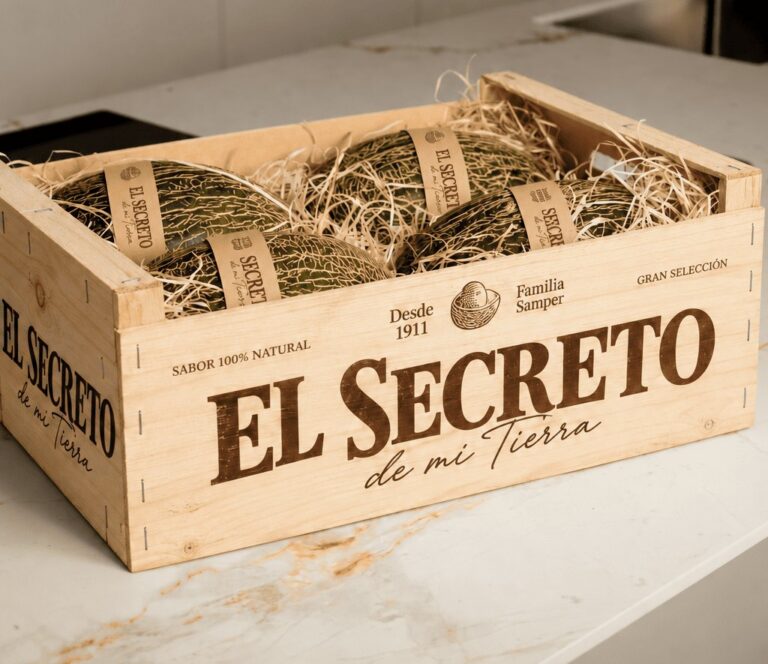 Melones envueltos en papel entre material de relleno, dentro de una caja de madera rotulada.