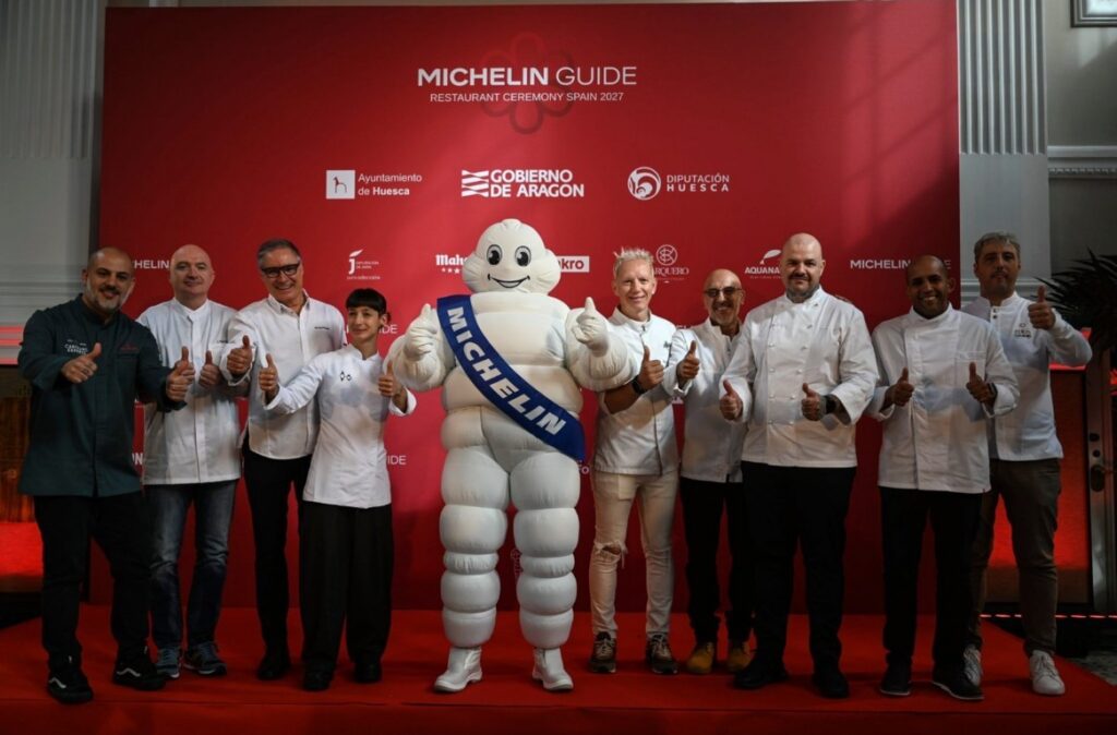 Grupo de personas junto a la mascota Michelin ante un fondo rojo de la Guía Michelin