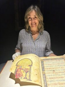 Una mujer con guantes sostiene un manuscrito abierto con texto e ilustraciones