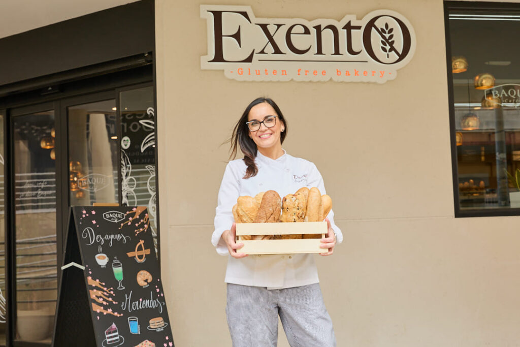 Mujer sostiene una caja de panes frente al letrero de Exento.