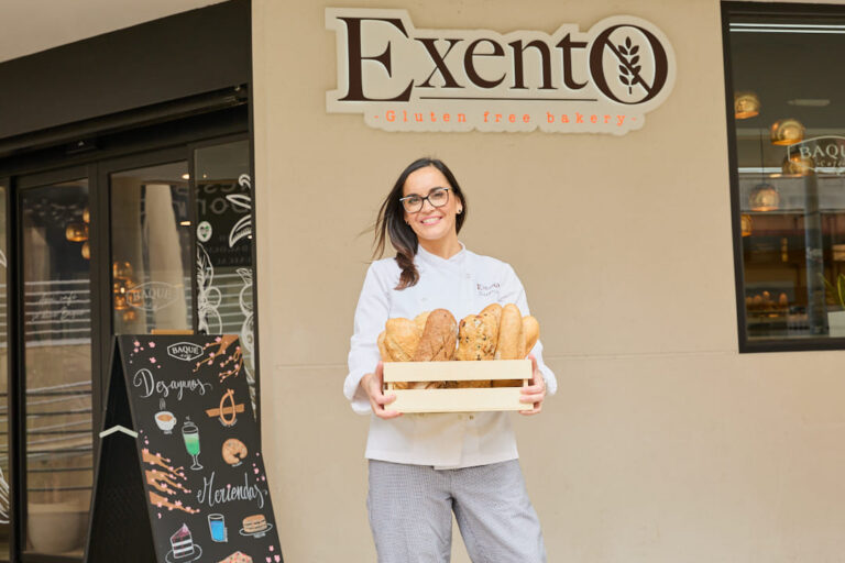 Mujer sostiene una caja de panes frente al letrero de Exento.