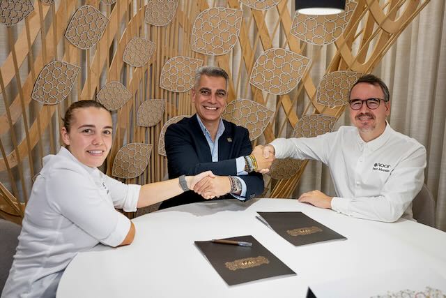 Tres personas estrechan las manos alrededor de una mesa en un comedor.