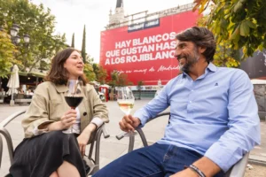 Dos personas conversan con copas de vino frente a un anuncio de Rioja en una terraza.