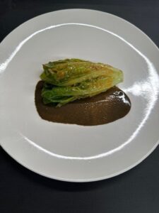 Verdura verde cocinada sobre una salsa oscura en un plato blanco