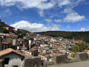 Vista de un pueblo en una ladera, con casas de tejados rojizos bajo nubes.
