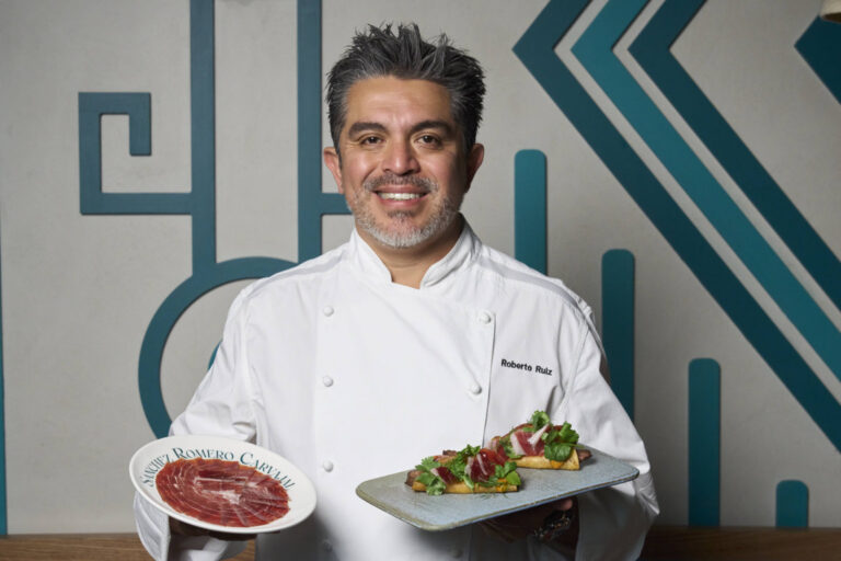 Roberto Ruiz sostiene un plato de jamón ibérico y una bandeja con comida.