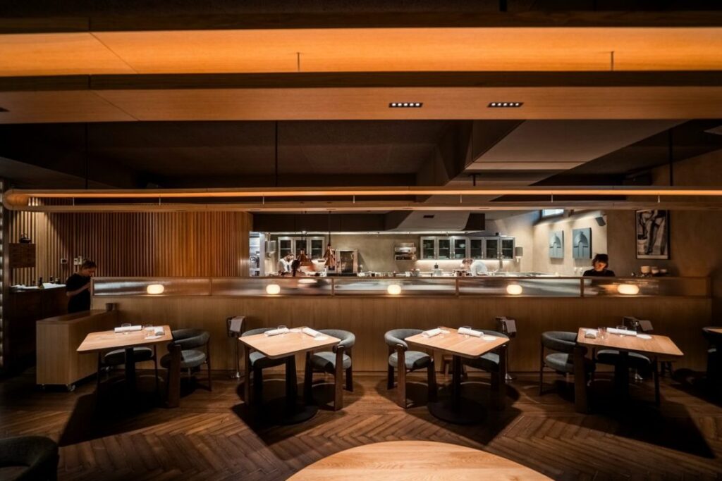 Sala de restaurante con mesas de comedor y cocina abierta al fondo.