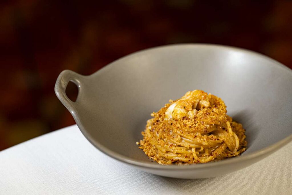 Plato de spaghetti con cigalas y migas tostadas servido en un cuenco gris