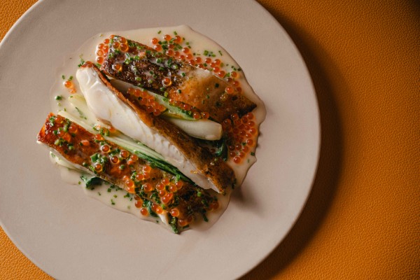 Rodaballo con beurre blanc y huevas naranjas, servido en un plato blanco.